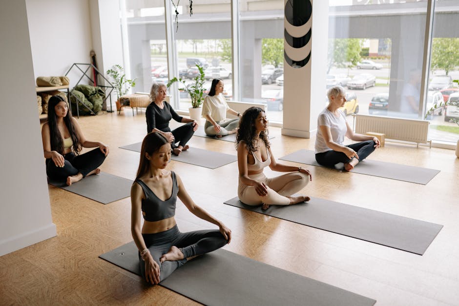 Group of people in a bright studio resting in a simple yoga pose.